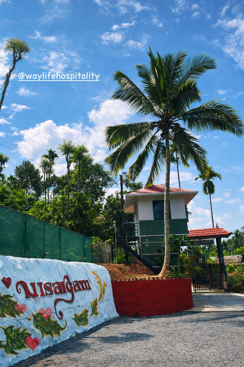 Nisargam entrance gateway framed by palms and tropical greenery